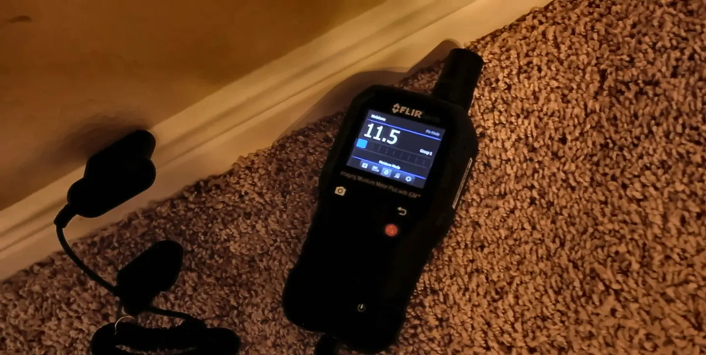 Technician taking a moisture reading on wet carpet, step one of what to do after water damage